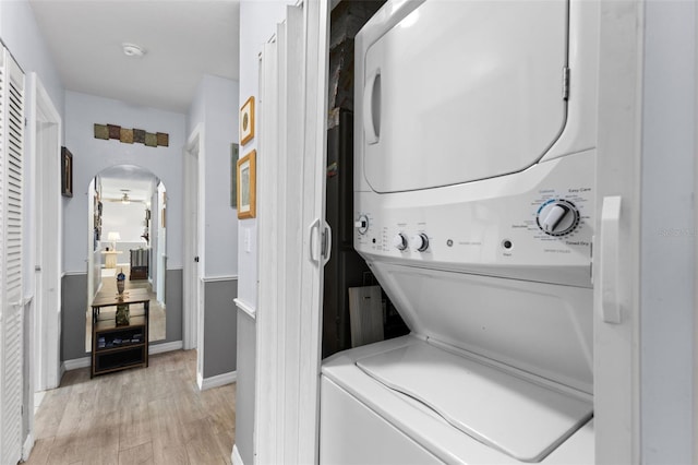 washroom with arched walkways, light wood finished floors, stacked washer / dryer, baseboards, and laundry area