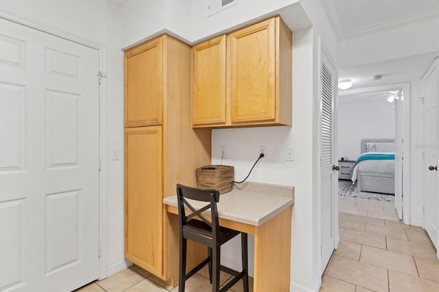 kitchen with light tile patterned floors, light countertops, crown molding, and light brown cabinetry