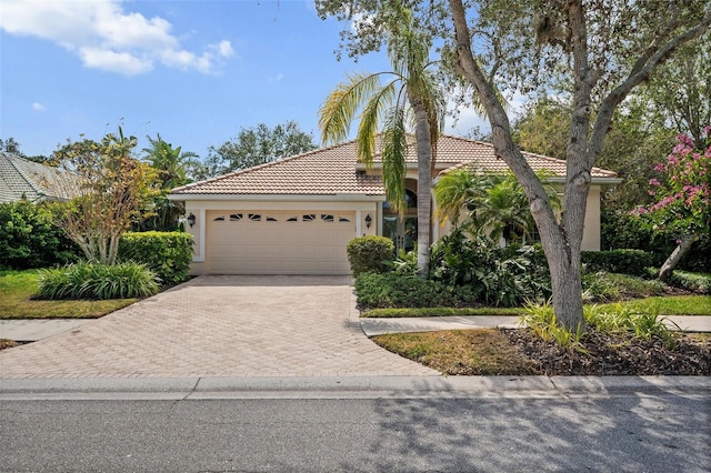 view of front facade featuring an attached garage, a tile roof, decorative driveway, and stucco siding