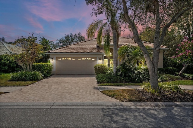 view of front of property with an attached garage, a tiled roof, decorative driveway, and stucco siding