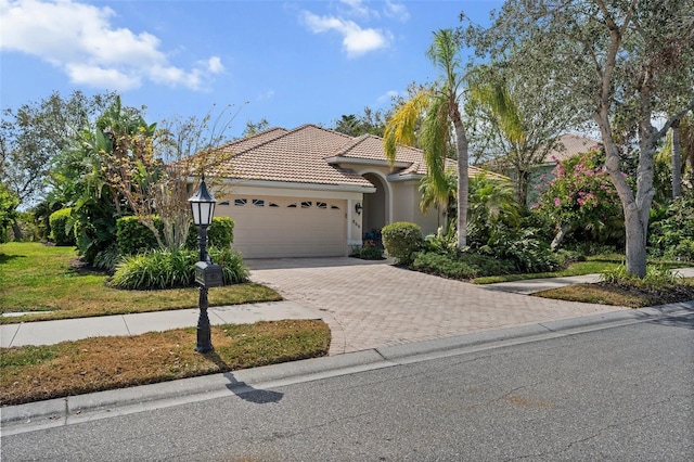 mediterranean / spanish-style house with an attached garage, a tile roof, decorative driveway, and stucco siding