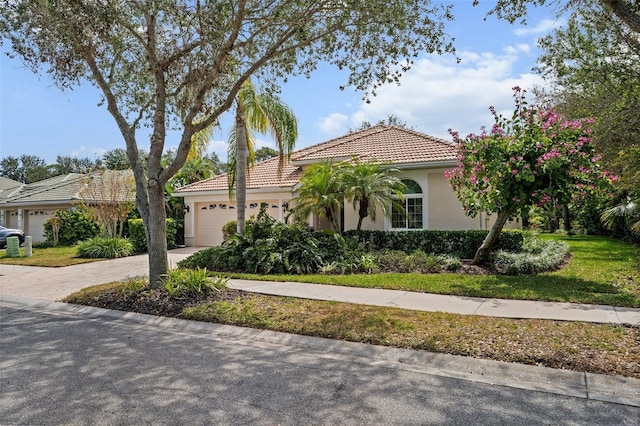 mediterranean / spanish-style house with a tiled roof, an attached garage, decorative driveway, a front lawn, and stucco siding