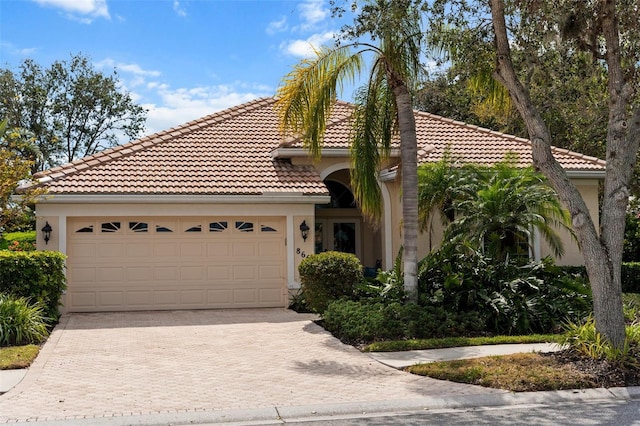 mediterranean / spanish-style home featuring a garage, decorative driveway, a tile roof, and stucco siding