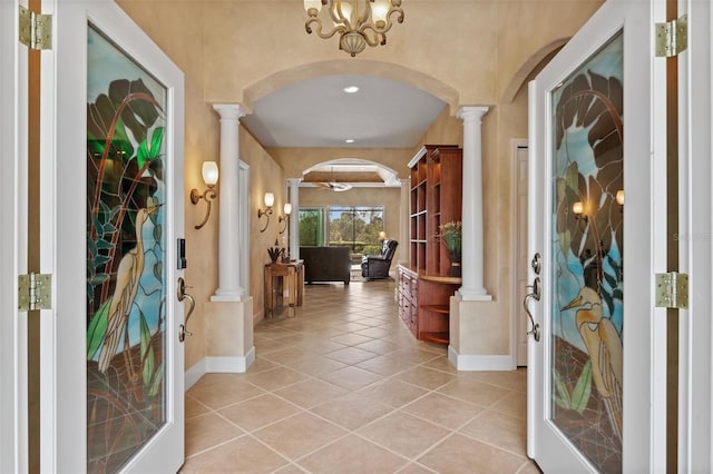 foyer entrance featuring light tile patterned floors, arched walkways, decorative columns, and baseboards