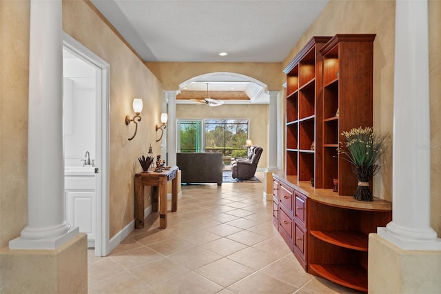 corridor with arched walkways, light tile patterned floors, ornate columns, a sink, and baseboards