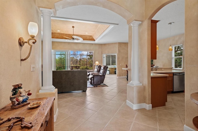 interior space featuring arched walkways, a tray ceiling, light tile patterned floors, a ceiling fan, and ornate columns