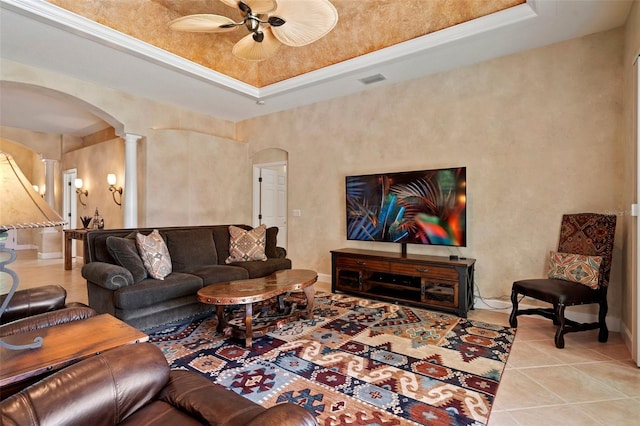 living room featuring arched walkways, ceiling fan, light tile patterned floors, a tray ceiling, and ornate columns