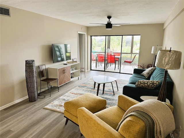 living area with light wood-type flooring, visible vents, baseboards, and ceiling fan