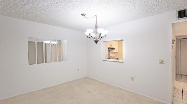 spare room featuring carpet floors, visible vents, a chandelier, and a textured ceiling