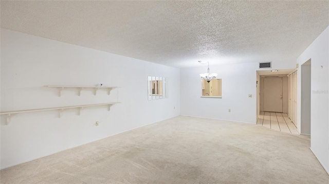 spare room with light carpet, a textured ceiling, a chandelier, and visible vents