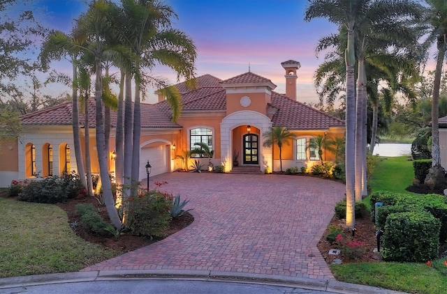 mediterranean / spanish-style house featuring stucco siding, a tile roof, decorative driveway, french doors, and an attached garage