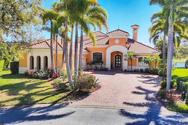 view of front of home with stucco siding, driveway, a front lawn, a tile roof, and french doors