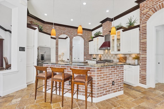 kitchen with a large island, wall chimney exhaust hood, appliances with stainless steel finishes, and stone tile flooring