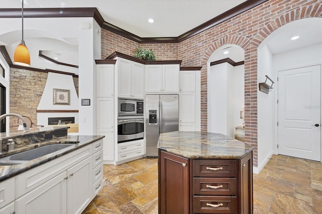 kitchen with stone tile flooring, ornamental molding, a sink, white cabinets, and appliances with stainless steel finishes