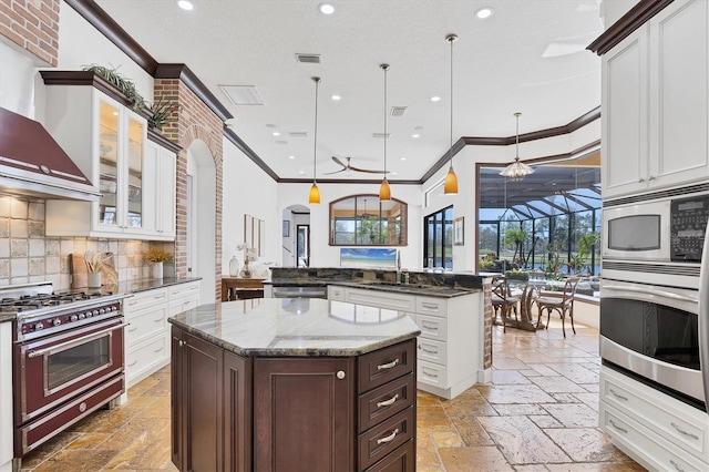 kitchen with visible vents, an island with sink, stone tile flooring, appliances with stainless steel finishes, and wall chimney range hood