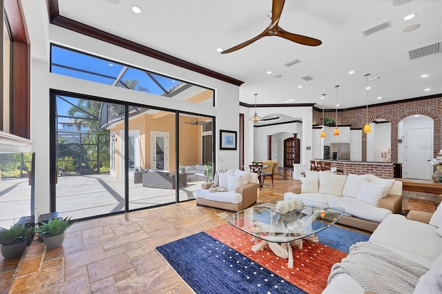 living room with arched walkways, visible vents, stone tile floors, and a ceiling fan