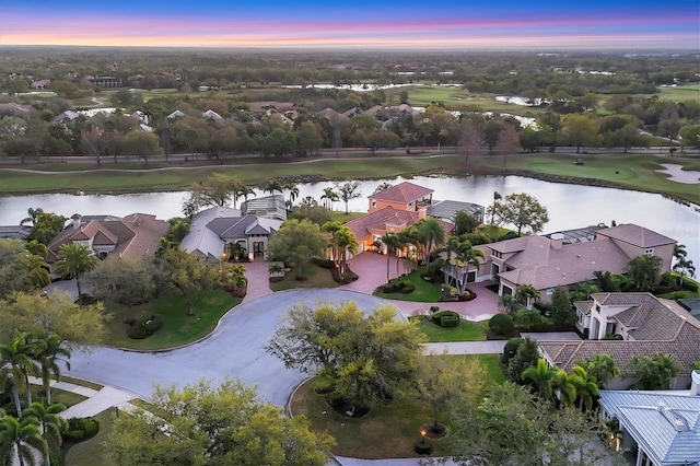 aerial view at dusk featuring a residential view, view of golf course, and a water view