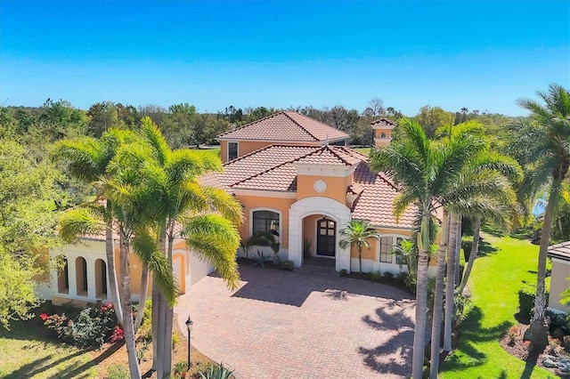 mediterranean / spanish home with a front yard, a tiled roof, decorative driveway, and stucco siding