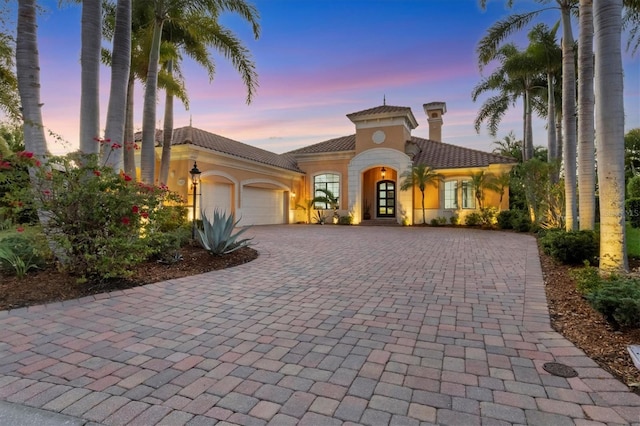 mediterranean / spanish-style home featuring decorative driveway, a garage, a chimney, and a tile roof