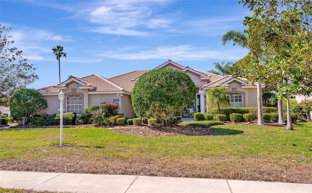 mediterranean / spanish house featuring a front lawn, a tiled roof, and stucco siding