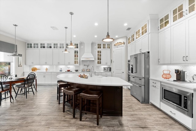 kitchen featuring premium range hood, light countertops, appliances with stainless steel finishes, tasteful backsplash, and an island with sink