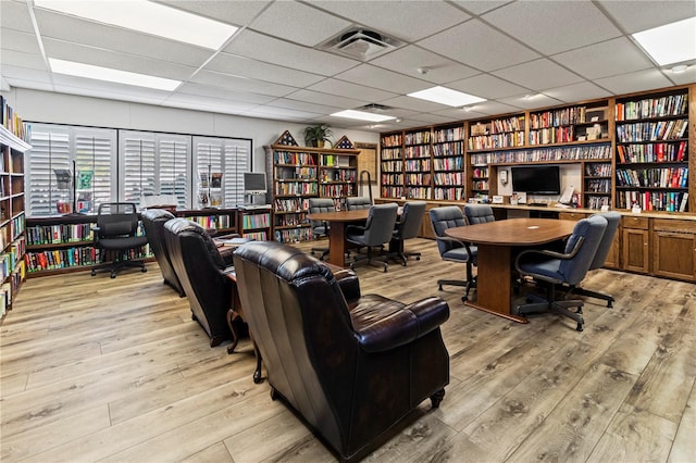 office area with light wood finished floors, bookshelves, a drop ceiling, and visible vents