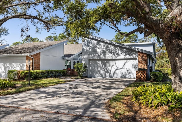 mid-century home with a shingled roof, concrete driveway, brick siding, and an attached garage