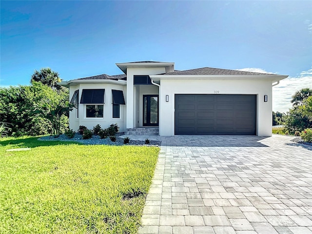 prairie-style home featuring a front lawn, decorative driveway, an attached garage, and stucco siding