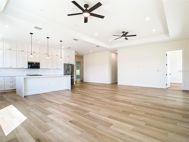 unfurnished living room with light wood finished floors, visible vents, a raised ceiling, baseboards, and ceiling fan