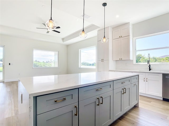 kitchen featuring gray cabinets, a raised ceiling, stainless steel dishwasher, light wood-style floors, and a sink