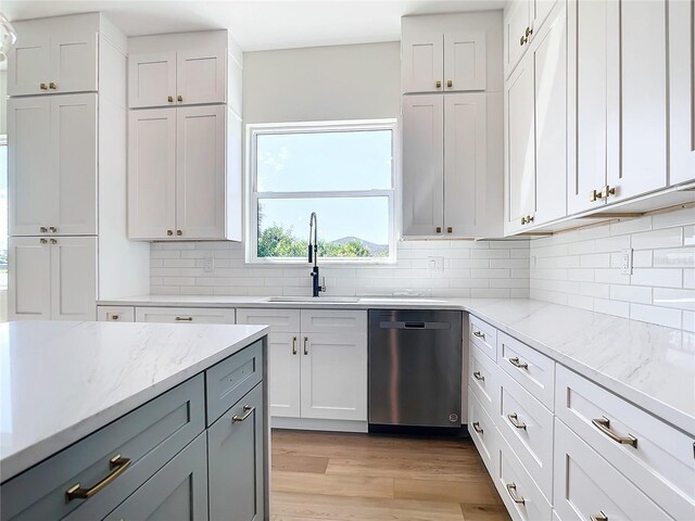 kitchen featuring light stone counters, a sink, stainless steel dishwasher, light wood finished floors, and tasteful backsplash