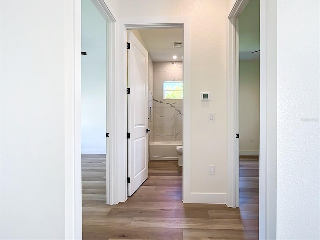 hallway featuring visible vents, baseboards, and wood finished floors