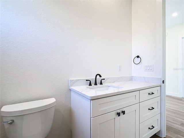 half bath featuring wood finished floors, vanity, and toilet