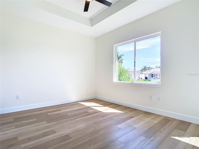 spare room featuring light wood-style floors, a raised ceiling, baseboards, and a ceiling fan