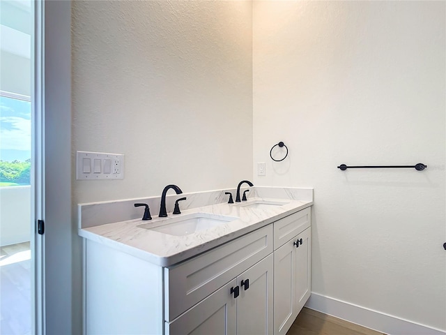 full bathroom featuring wood finished floors, a sink, baseboards, and double vanity