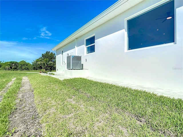 view of side of property featuring a lawn, cooling unit, and stucco siding