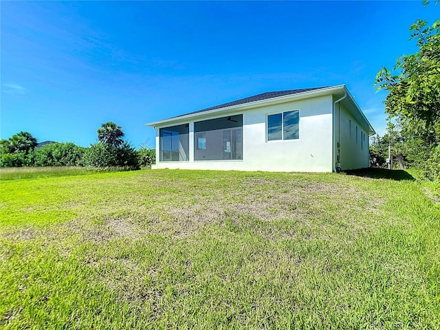 rear view of property featuring a sunroom, a lawn, and stucco siding