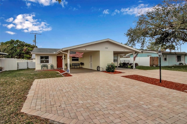 view of front facade featuring an attached carport, fence, stucco siding, a front lawn, and decorative driveway