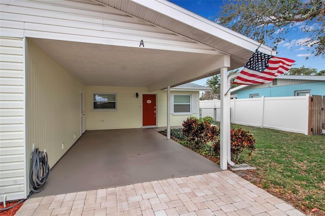 view of exterior entry with a yard, a carport, and fence