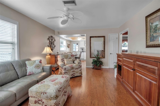 living room with visible vents, baseboards, light wood-style floors, and ceiling fan