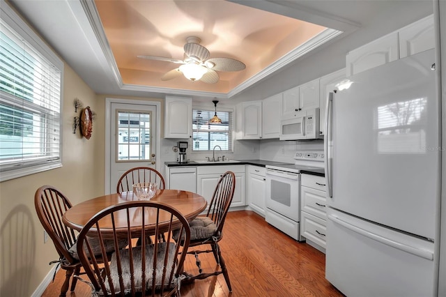 kitchen with light wood-style flooring, a sink, a tray ceiling, dark countertops, and white appliances