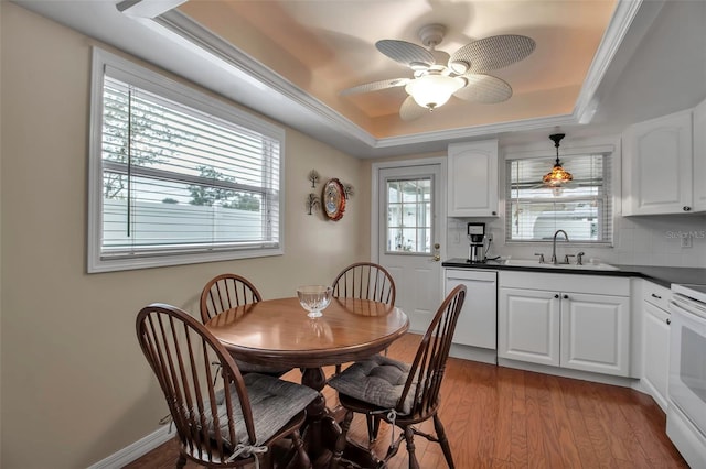 dining area with crown molding, baseboards, a tray ceiling, light wood-style floors, and a ceiling fan