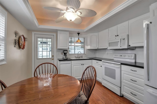 kitchen with a sink, dark countertops, wood finished floors, white appliances, and a raised ceiling