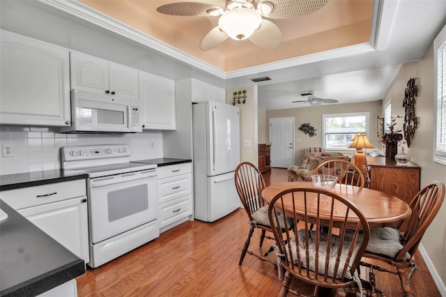 kitchen featuring dark countertops, backsplash, light wood-type flooring, a tray ceiling, and white appliances