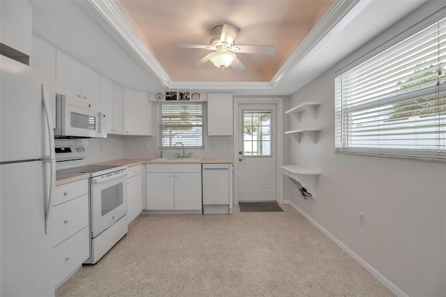 kitchen with white appliances, baseboards, a tray ceiling, a sink, and white cabinets