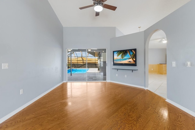 unfurnished living room featuring arched walkways, ceiling fan, wood finished floors, and baseboards