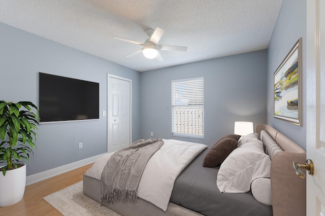 bedroom with ceiling fan, a textured ceiling, baseboards, and wood finished floors