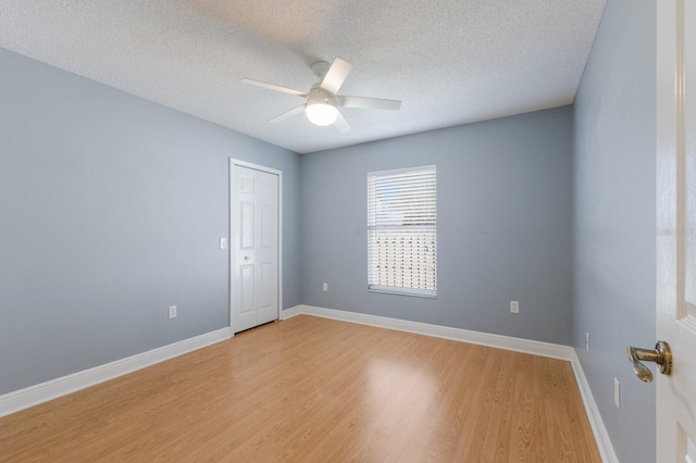 empty room featuring ceiling fan, a textured ceiling, light wood-style flooring, and baseboards