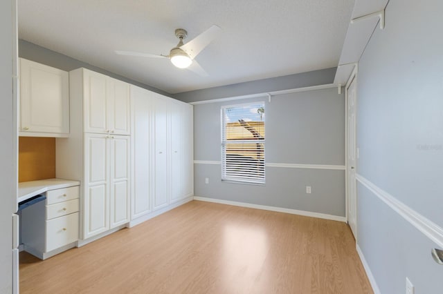 interior space featuring baseboards, white cabinets, light countertops, light wood-type flooring, and built in desk