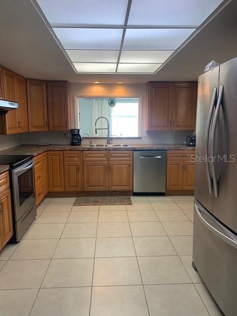 3013 Yarmouth Dr W, Bradenton, FL 34205 - kitchen with stainless steel appliances, extractor fan, light tile patterned floors, and brown cabinetry